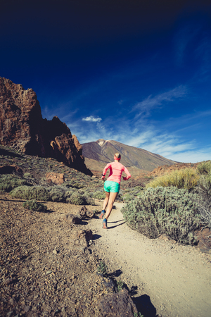 Young woman trail running in mountains on sunny summer day. Female runner jogging and working out in nature, cross country running on rocky trail footpath on Tenerife, Canary Islandsの写真素材