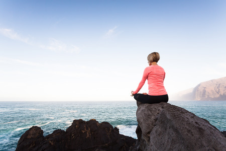 Woman meditating in yoga pose, ocean view, beach and rock mountains. Motivation and inspirational fit and exercising. Healthy lifestyle outdoors in nature concept.の写真素材