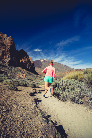 Young woman trail running in mountains on sunny summer day. Female runner jogging and working out in nature, cross country running on rocky trail footpath on Tenerife, Canary Islandsの写真素材