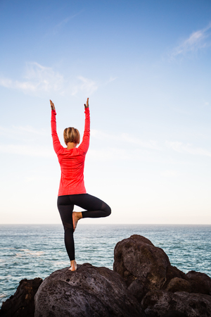 Yoga girl meditating in yoga vrksasana tree pose silhouette at the ocean, beach and rock mountains. Motivation and inspirational fit and exercising. Healthy lifestyle outdoors in nature, fitness concept.の写真素材