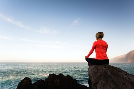 Woman meditating in yoga pose, ocean view, beach and rock mountains. Motivation and inspirational fit and exercising. Healthy lifestyle outdoors in nature concept.の写真素材