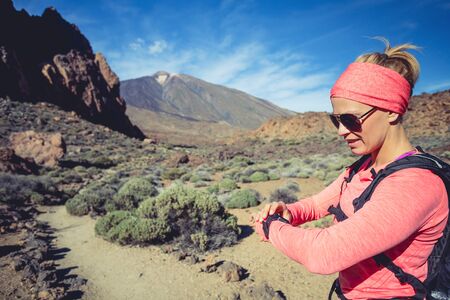 Trail running woman on mountain trail looking at sportwatch, checking performance, heart pulse or GPS position nd track. Cross country running in beautiful nature, Canary Islands.の写真素材
