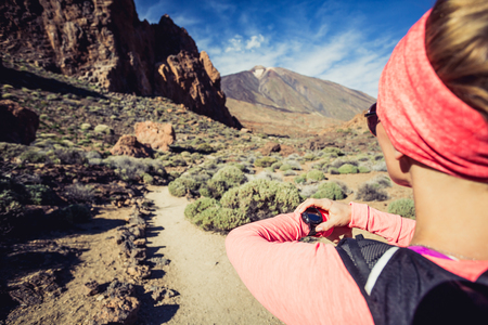 Trail running woman on mountain trail looking at sportwatch, checking performance, heart pulse or GPS position nd track. Cross country running in beautiful nature, Canary Islands.の写真素材