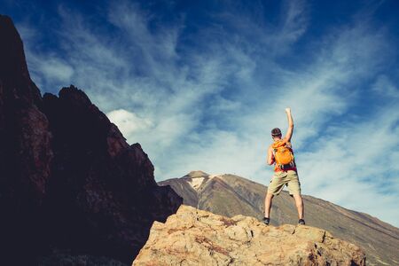 Man with arms outstretched celebrating beautiful inspiring view in mountains. Male hiker or climber with hands up enjoy inspirational landscape on rocky trail on Tenerife, Canary Islands.の写真素材
