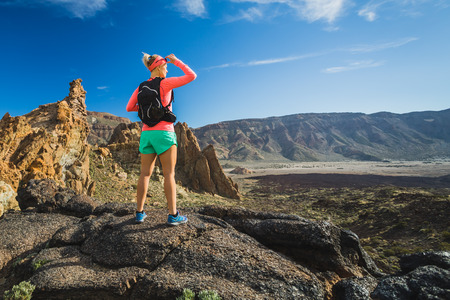 Woman hiker reached mountain top. Inspire and motivate concept for outdoors activity. Female runner or climber looking at inspirational landscape on rocky trail on Tenerife, Canary Islands Spain.の写真素材