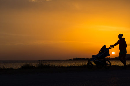 Mother walking on beach with stroller enjoying motherhood at sunset landscape. Jogging or power...