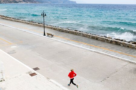 Happy girl running on city street at seaside. Young athlete training and doing workout in urban scene. Sport and fitness inspiration and motivation. Vintage tone.の写真素材