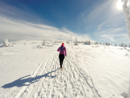Running woman on winter trail, snow and white mountains. Young happy girl with backpack cross country running in mountains. Female trail runner jogging exercising outdoors.の写真素材