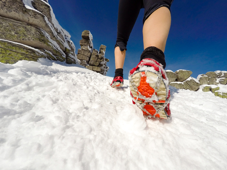 Running woman on winter trail, snow and white mountains. Young happy girl with backpack cross country running in mountains. Female trail runner jogging exercising outdoors.の写真素材