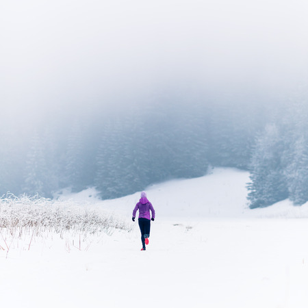 Woman trail running in mountains on snow footpath, winter day. Sport, fitness inspiration and motivation. Girl cross country runner training in cold conditions.の写真素材