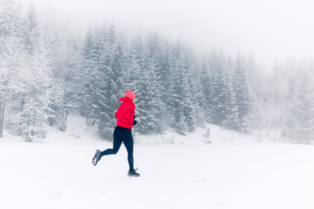 Girl running on snow in winter mountains. Sport, fitness inspiration and motivation. Young happy woman trail running in mountains on snow, winter day. Female trail runner jogging outdoors.の写真素材