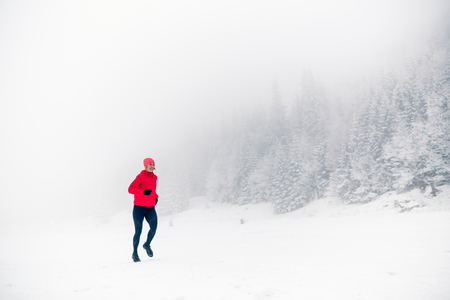 Winter running woman on snow in white mountains and forest. Sport, fitness inspiration and motivation. Young happy girl athlete working out on snow, winter day. Female runner jogging outdoors.の写真素材