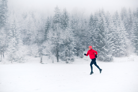 Girl running on snow in winter mountains. Sport, fitness inspiration and motivation. Young happy woman trail running in mountains on snow, winter day. Female trail runner jogging outdoors.の写真素材