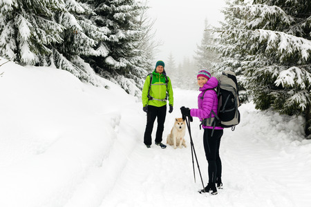 Man and woman happy teamwork couple hikers trekking in white winter woods and mountains. Young people walking on snowy trail with backpacks, healthy lifestyle adventure, camping and hiking, Poland.の写真素材