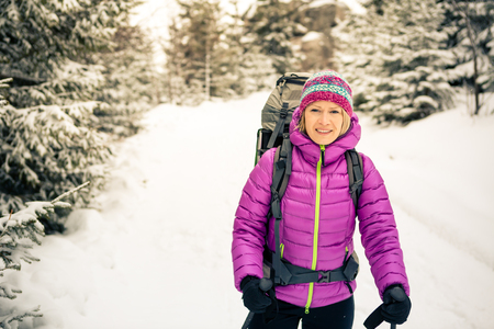 Woman hiking in white winter forest woods with backpack. Recreation fitness and healthy lifestyle outdoors in nature, camping outdoors. Motivation and inspirational winter landscape.の写真素材