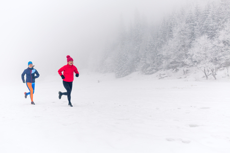 Girls running together on snow in winter mountains. Sport, fitness inspiration and motivation. Two women partners trail running in mountains, winter day. Female trail runner jogging outdoors.の写真素材