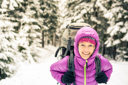 Woman hiking in white winter forest woods with backpack. Young girl walking on snowy trail. Recreation fitness and healthy lifestyle, camping outdoors. Motivation and inspirational winter landscape.の写真素材