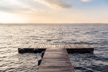 Peaceful scene with empty wooden bridge in the morning sun. Endless lake with small waves with reflecting sunlight.の写真素材