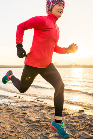 Woman beach running at sunrise, lake coastline. Training and working out, runner jogging and exercising outdoors in a morning sun.の写真素材