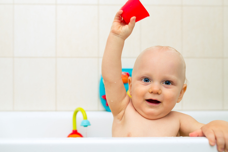 Baby boy taking a bath, playing in a bathtub with colorful toys. Smiling little kid in bathroom looking at camera. Infant playing, have fun and washing. Healthy hygiene and care for children.の写真素材