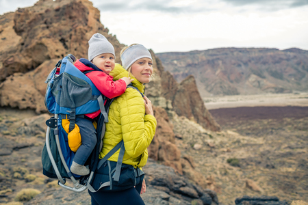 Family hike baby boy travelling in mother's backpack. Hiking adventure with child on autumn family trip in mountains. Vacations journey with infant carried on back, weekend travel in Tenerife, Spain.の写真素材