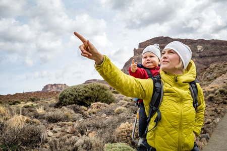 Super mom with baby boy travelling in backpack. Mother on hiking adventure with child, family trip in mountains. Vacations journey with infant carried on back, weekend travel in Tenerife, Spain.の写真素材