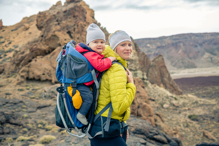 Family hike baby boy travelling in mother's backpack. Hiking adventure with child on autumn family trip in mountains. Vacations journey with infant carried on back, weekend travel in Tenerife, Spain.の写真素材