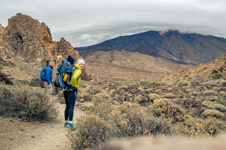 Couple hiking with baby boy travelling in backpack. Hiking adventure with child on autumn family trip in mountains. Family vacations with infant carried on back, weekend travel in Tenerife, Spain.の写真素材
