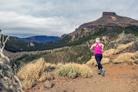 Trail running girl in mountains on rocky path. Cross country runner training in inspiring nature, dirt footpath on Tenerife, Canary Islands Spain.の写真素材