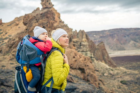 Family hike baby boy travelling in mother's backpack. Hiking adventure with child on autumn family trip in mountains. Vacations journey with infant carried on back, weekend travel in Tenerife, Spain.の写真素材