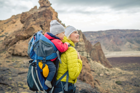 Family hike baby boy travelling in mother's backpack. Hiking adventure with child on autumn family trip in mountains. Vacations journey with infant carried on back, weekend travel in Tenerife, Spain.の写真素材