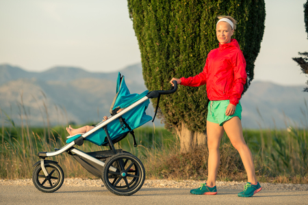 Mother with child in baby stroller enjoying summer sunset and mountains landscape. Jogging or power walking woman with pram. Beautiful inspirational mountains landscape.の写真素材