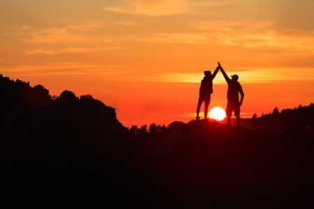 Teamwork couple celebrating silhouette in inspiring mountains sunset. Team of climbers celebrate reached goal and success. Achievement and motivation concept on top of mountain, Corsica France.の写真素材