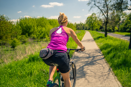 Woman cycling a mountain bike in a city park, summer day. Inspire and motivate concept for outdoors activity. Girl cyclist smiling and riding bicycle on a dirt road.の写真素材