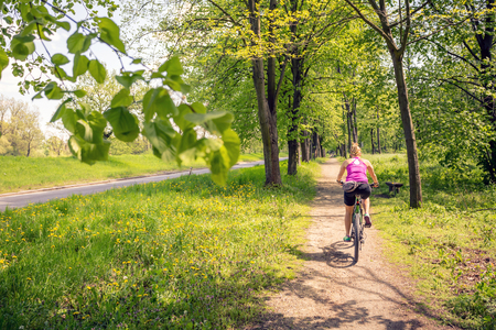 Woman cycling a mountain bike in a city park, summer day. Inspire and motivate concept for outdoors activity. Girl cyclist smiling and riding bicycle on a dirt road.の写真素材