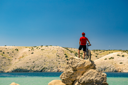 Mountain biker looking at view and traveling on bike in summer sea landscape. Man riding a bicycle in mountains and beach. Fitness motivation, inspiration in beautiful inspirational view.の写真素材