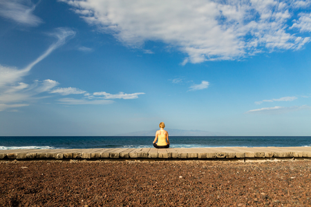 Woman meditating in yoga pose, ocean view, beach and wooden sidewalk. Motivation and inspirational summer sea landscape. Healthy lifestyle outdoors in nature concept.の写真素材