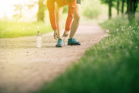 Woman runner tying sport shoes. Walking or running legs, autumn adventure and exercising outdoors. Motivation and inspiration fitness concept outside.の写真素材