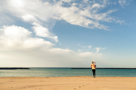 Mother with baby boy enjoy sunrise on a beach. Walking and relaxing woman holding baby boy toddler. Beautiful inspirational beach and ocean landscape.の写真素材