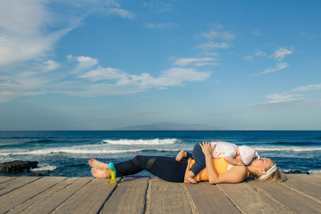 Baby boy playing with mother on the beach, summer day. Supermom with toddler son relaxing on wooden beach sidewalk. Looking at inspiring landscape.の写真素材