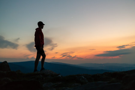 Man celebrating sunset on mountain top. Looking at inspiring view. Trail runner, hiker or climber...