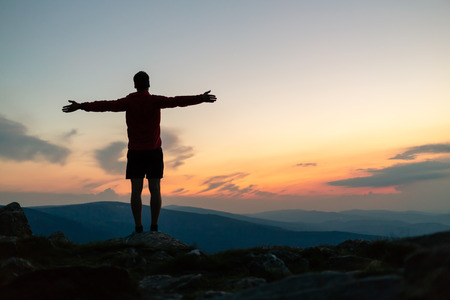 Man celebrating sunset on mountain top. Looking at inspiring view. Trail runner, hiker or climber reached mountain peak, enjoy inspirational landscape on rocky trail Karkonosze, Polandの写真素材