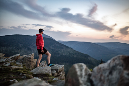 Man celebrating sunset looking at view in mountains. Trail runner, hiker or climber reached top of a mountain, enjoy inspirational landscape on rocky trail Karkonosze, Polandの写真素材