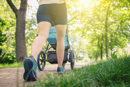 Walking woman with baby stroller enjoying summer day in park. Jogging or power walking supermom, active family with baby jogger.の写真素材
