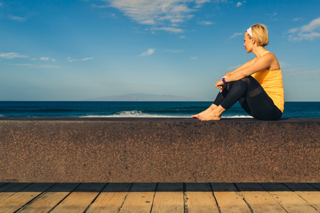 Woman meditating in yoga pose, ocean view, beach and wooden sidewalk. Motivation and inspirational summer sea landscape. Healthy lifestyle outdoors in nature concept.の写真素材