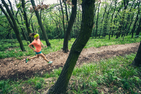 Young woman running in green forest. Endurance sport training. Female trail runner cross country running. Sport and fitness concept outdoors in nature.の写真素材