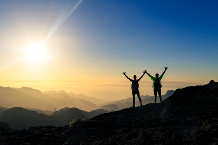 Couple hikers success and trust in mountains, accomplish with arms up outstretched. Young man and woman looking at beautiful inspirational landscape view, Gran Canaria Canary Islands.の写真素材