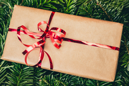 Christmas gift on green pine or spruce tree. Red ribbon on paper gift box. Top closeup view with copy space.の写真素材