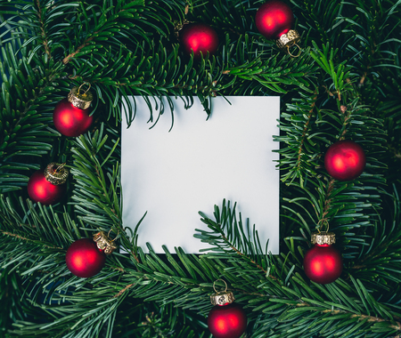 Christmas card note on green spruce tree branches with red balls. Top closeup view with copy space.の写真素材