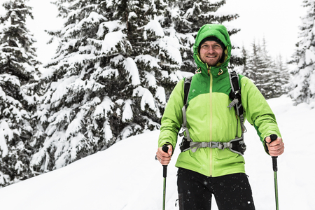 Smiling man walking on winter trek in white snowy forest, looking at camera. Man hiking in winter woods. Travel and healthy lifestyle outdoors in beautiful nature.の写真素材